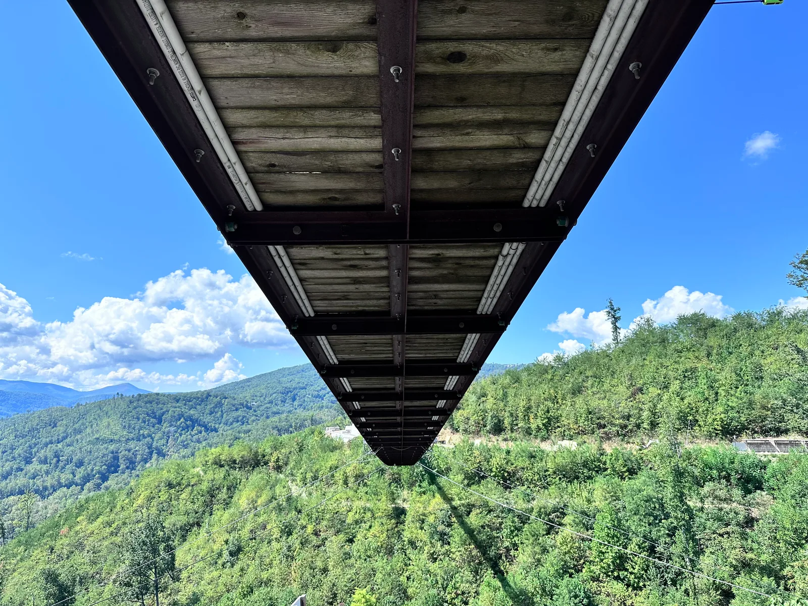 View beneath the suspended wooden deck of the Gatlinburg SkyBridge with wooded hills beyond
